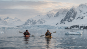 Two kayakers paddling among Antarctic ice and mountains